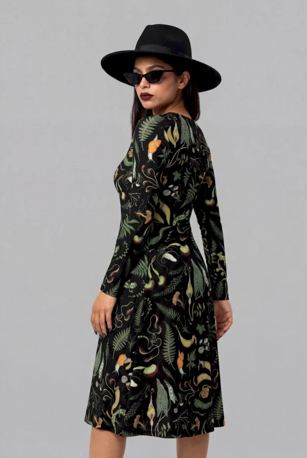 A woman in the Cosmic Drifters Werewood Long Sleeve Midi Dress, featuring a forest print with animal motifs, pairs it with a black wide-brimmed hat and sunglasses while standing against a plain gray background.