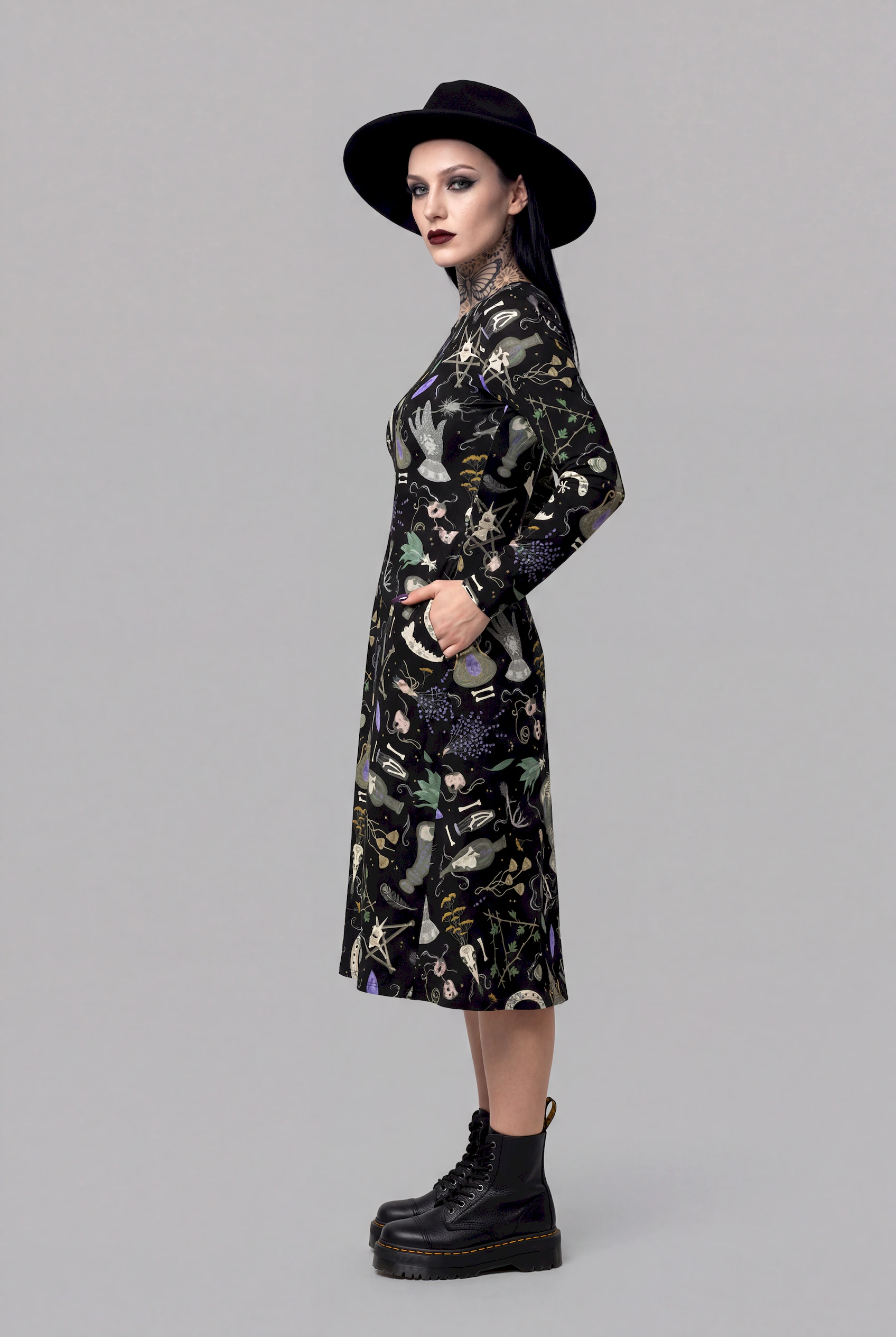 A woman in the Cosmic Drifters Witches Altar Long Sleeve Midi Dress and black platform boots stands sideways against a plain gray background.